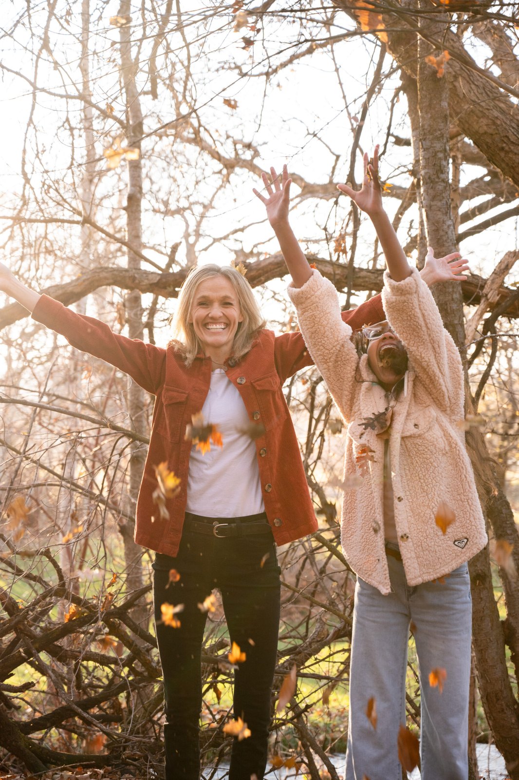 Two women tossing autumn leaves beneath bare trees