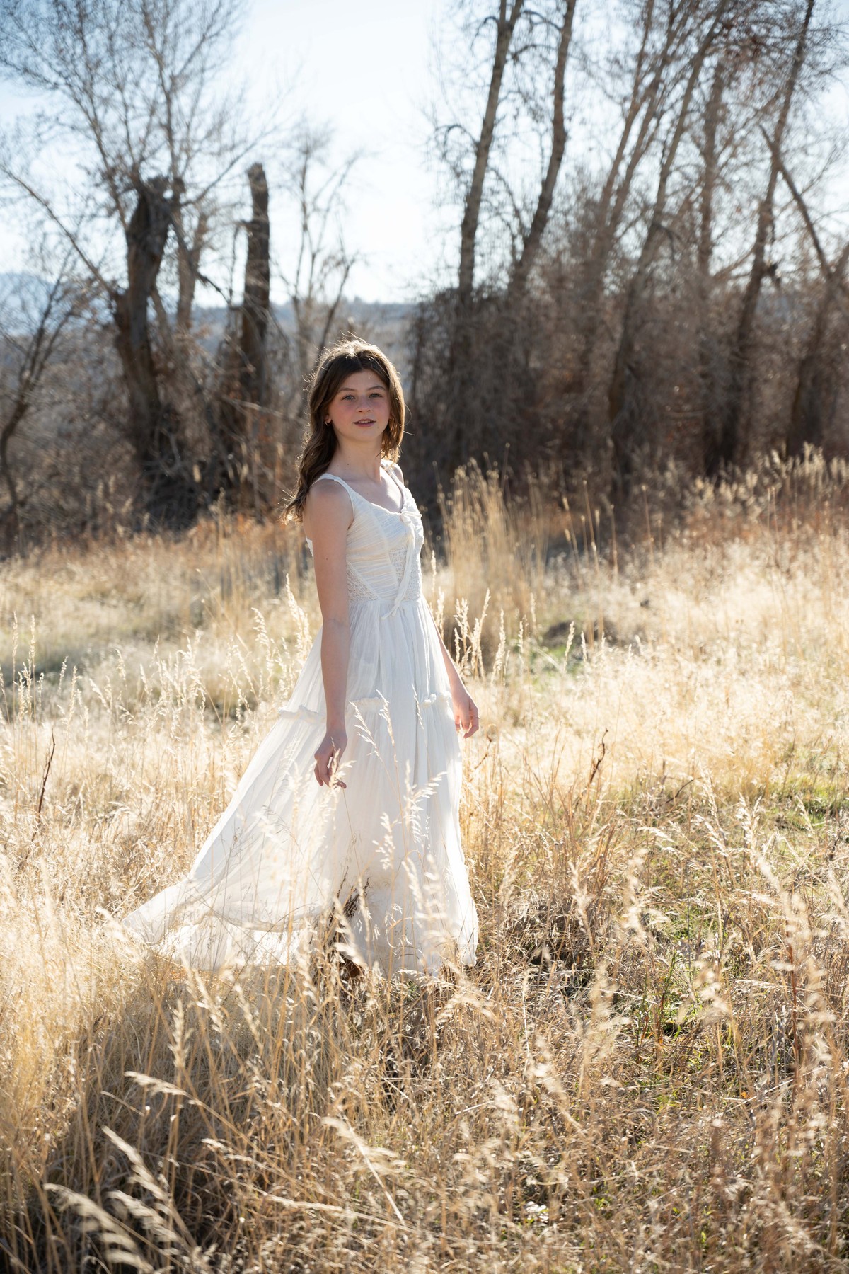 Bride in a white dress walking through sunlit meadow grass